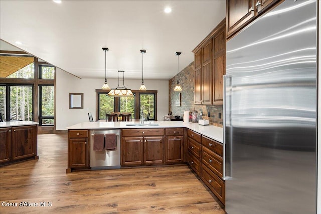 kitchen featuring a peninsula, light countertops, a sink, stainless steel appliances, and backsplash