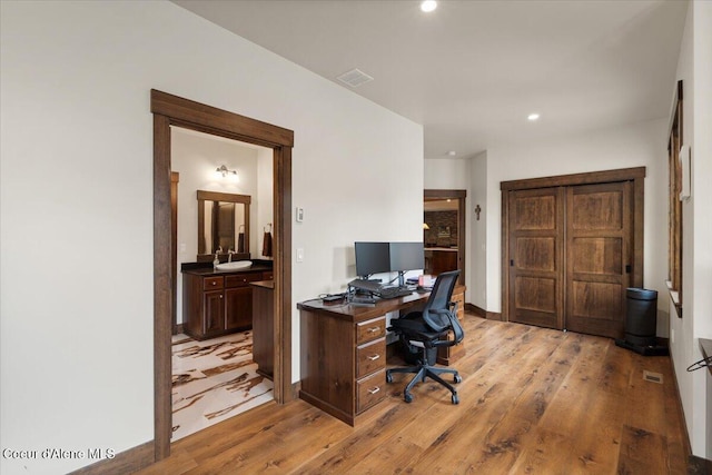 office space with light wood-style flooring, visible vents, recessed lighting, a sink, and baseboards