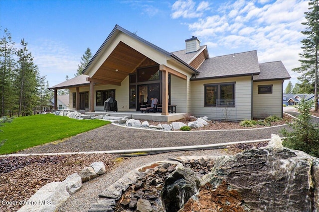 back of property with a patio, a chimney, roof with shingles, and a yard