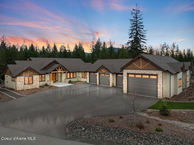 view of front of property with an attached garage, stone siding, driveway, and roof with shingles
