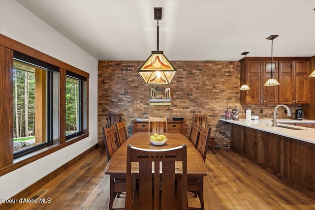 dining space featuring brick wall, wood-type flooring, and baseboards