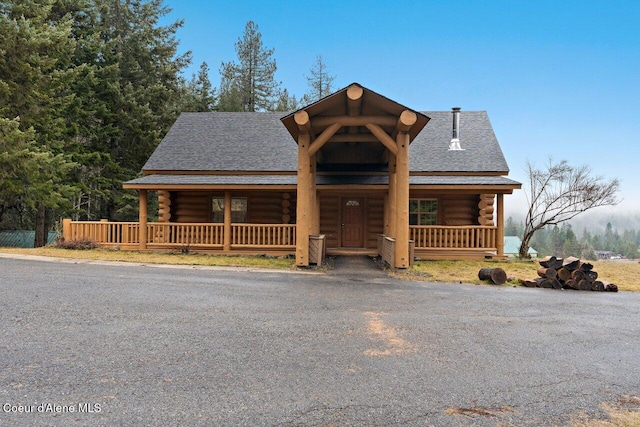 log-style house featuring log exterior, a porch, and roof with shingles