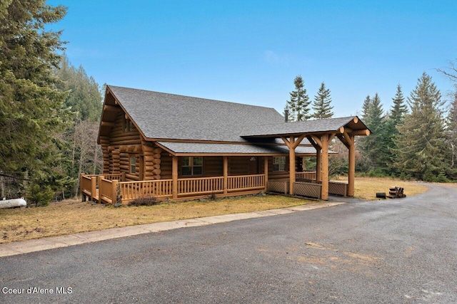 view of front of house with a porch, a shingled roof, and log exterior
