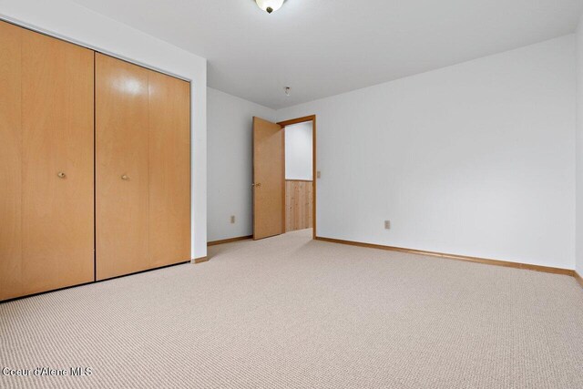 unfurnished bedroom featuring baseboards, light carpet, and a closet