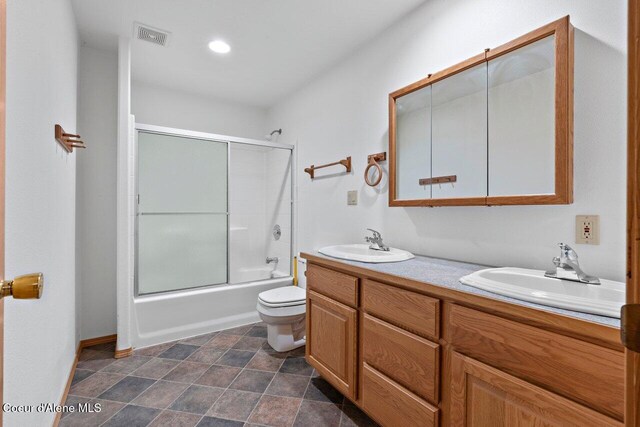 bathroom featuring combined bath / shower with glass door, toilet, double vanity, and a sink