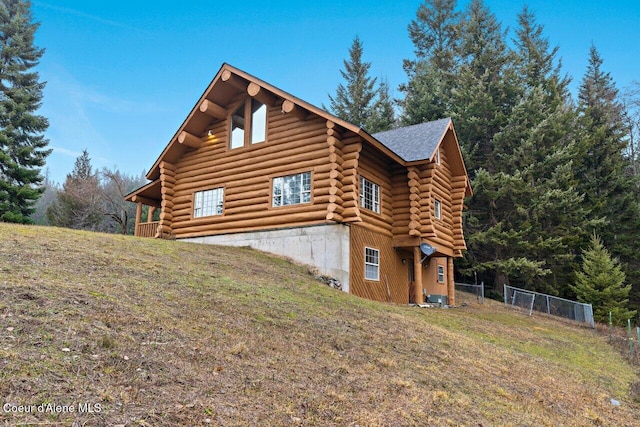 view of home's exterior with a yard, fence, roof with shingles, central AC, and log siding