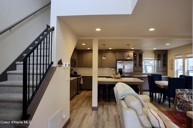 kitchen with light wood-type flooring, visible vents, appliances with stainless steel finishes, light countertops, and a center island with sink