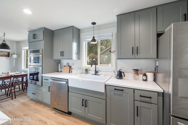 kitchen with gray cabinets, appliances with stainless steel finishes, decorative light fixtures, and a sink