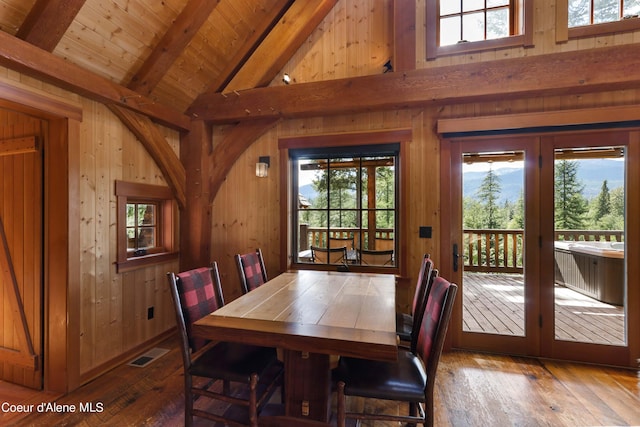 dining space featuring wooden walls, visible vents, hardwood / wood-style floors, beamed ceiling, and wood ceiling