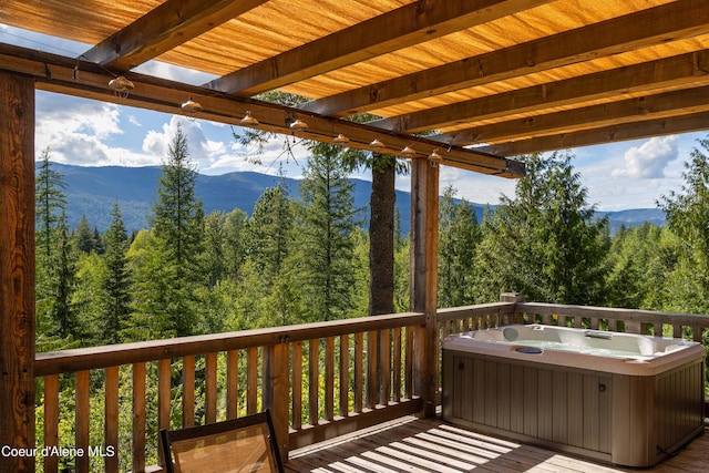 wooden terrace featuring a forest view, a mountain view, and a hot tub