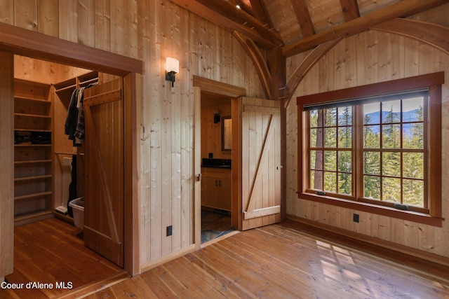 interior space featuring wood-type flooring, a closet, wooden walls, and lofted ceiling with beams