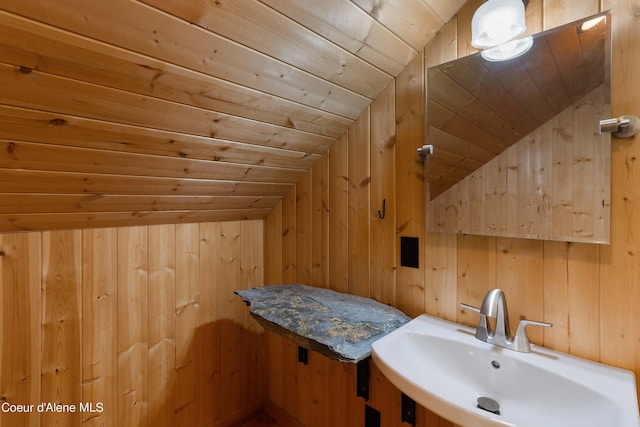 bathroom featuring wood ceiling, wooden walls, a sink, and vaulted ceiling