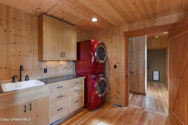 laundry area with stacked washer and dryer, cabinet space, light wood finished floors, wood ceiling, and a sink
