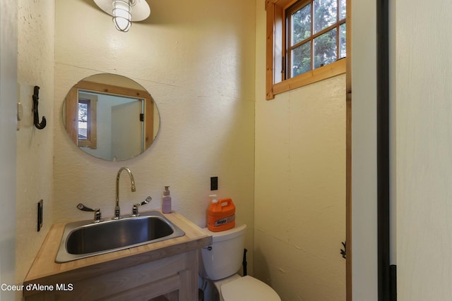 bathroom with toilet, vanity, and a textured wall