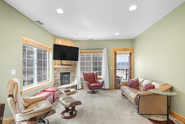 carpeted living area with visible vents, a stone fireplace, recessed lighting, and baseboards