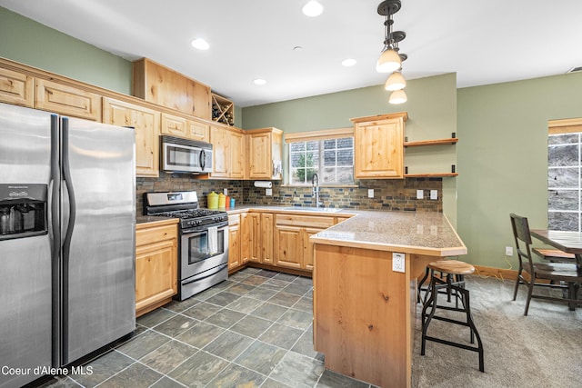 kitchen with light brown cabinets, a sink, appliances with stainless steel finishes, a peninsula, and a breakfast bar area