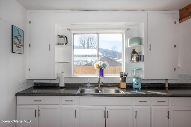 kitchen featuring tasteful backsplash, white cabinetry, a sink, and dark countertops