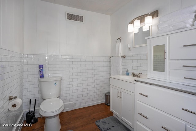 bathroom featuring vanity, visible vents, toilet, wood finished floors, and tile walls