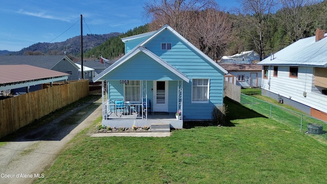 rear view of property featuring a mountain view, covered porch, a lawn, fence, and driveway