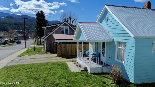 view of property exterior with a porch, a chimney, metal roof, and a yard
