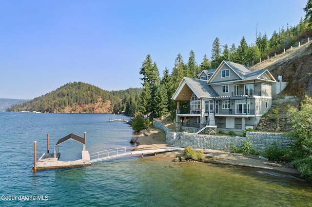 dock area with a water view, stairs, a balcony, and a view of trees