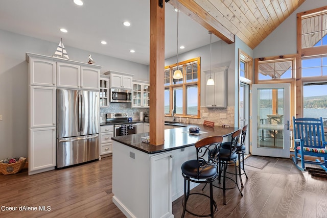 kitchen featuring dark wood-style flooring, a peninsula, white cabinetry, dark countertops, and appliances with stainless steel finishes