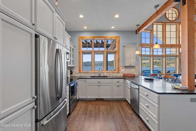 kitchen with recessed lighting, a peninsula, dark countertops, appliances with stainless steel finishes, and a sink
