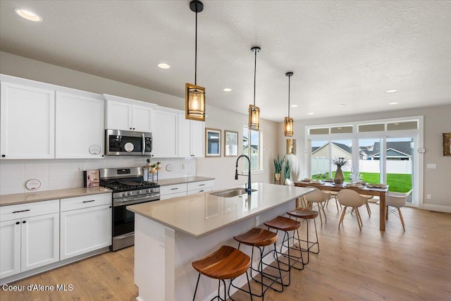 3402 N Cyprus Fox Loop, Post Falls, ID 83854 - kitchen featuring a kitchen island with sink, tasteful backsplash, a sink, light wood-style flooring, and appliances with stainless steel finishes
