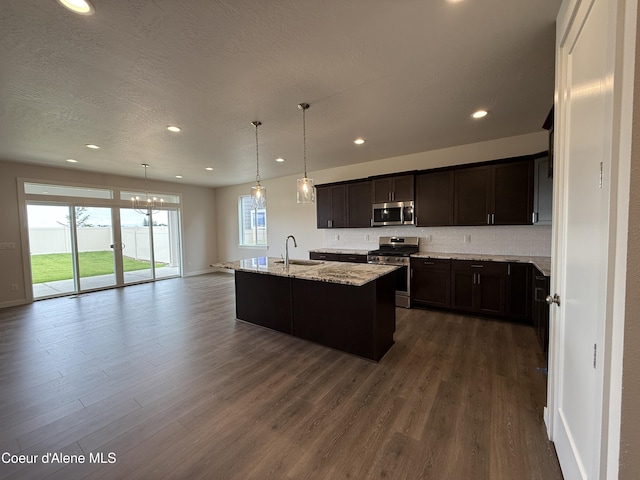 3402 N Cyprus Fox Loop, Post Falls, ID 83854 - kitchen featuring appliances with stainless steel finishes, dark wood-style floors, tasteful backsplash, a center island with sink, and light stone countertops