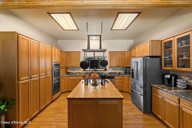 kitchen featuring glass insert cabinets, a center island, stainless steel appliances, butcher block countertops, and light wood-style flooring