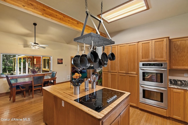 kitchen with brown cabinets, double oven, wood counters, light wood finished floors, and black electric stovetop
