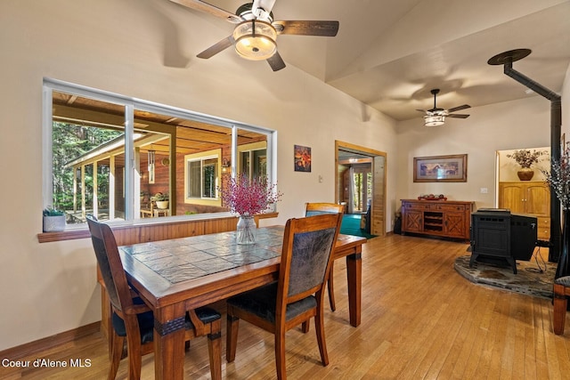 dining room featuring a wood stove, light wood-type flooring, vaulted ceiling, and ceiling fan
