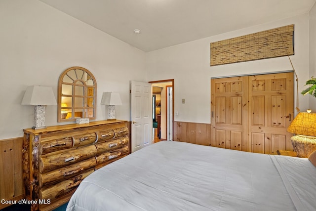 bedroom featuring wooden walls, wainscoting, and lofted ceiling