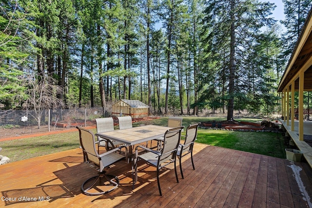 wooden deck featuring an outbuilding, outdoor dining space, fence, and a lawn