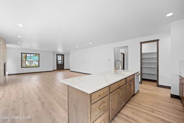 kitchen featuring light wood-type flooring, light stone counters, an island with sink, white dishwasher, and a sink