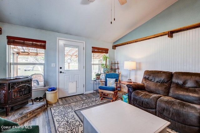 living area with a wood stove, wood finished floors, a ceiling fan, and lofted ceiling