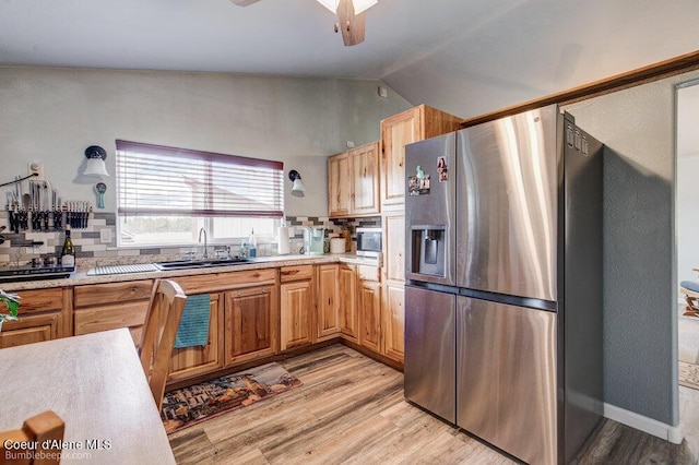 kitchen featuring a sink, light wood-type flooring, stainless steel appliances, decorative backsplash, and lofted ceiling