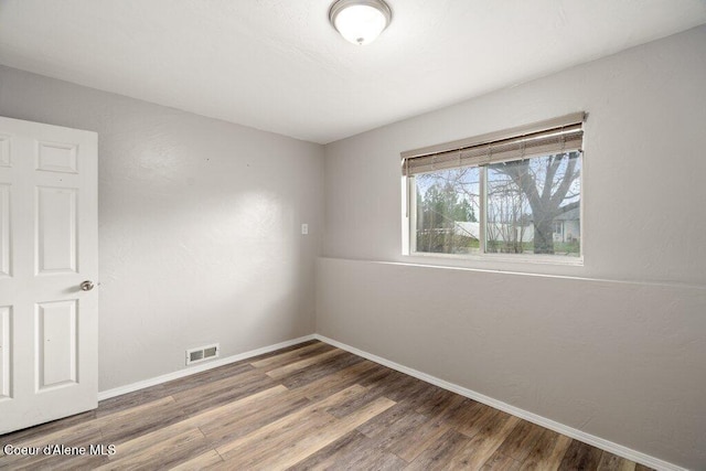 empty room with wood finished floors, baseboards, and visible vents