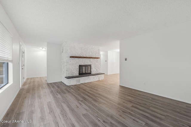 unfurnished living room with a textured ceiling, wood finished floors, and a stone fireplace