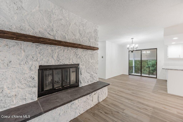 unfurnished living room with a fireplace, an inviting chandelier, a textured ceiling, and wood finished floors