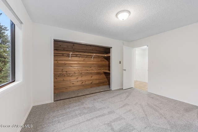 unfurnished bedroom featuring multiple windows, a textured ceiling, a closet, and carpet floors