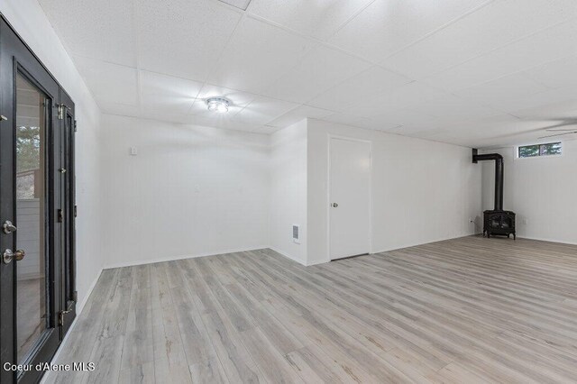 basement with a drop ceiling, a wood stove, and wood finished floors