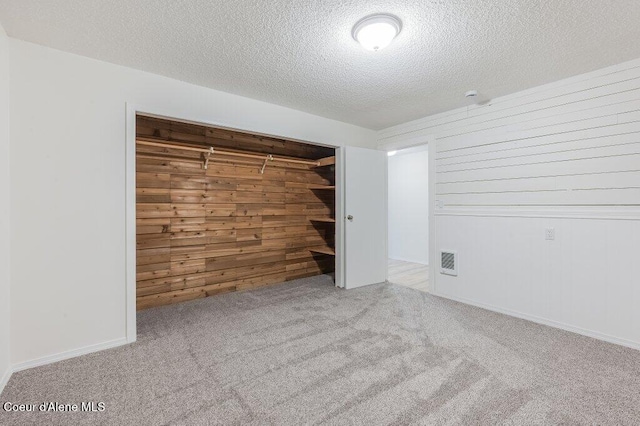 spare room featuring a textured ceiling, carpet floors, wooden walls, and visible vents