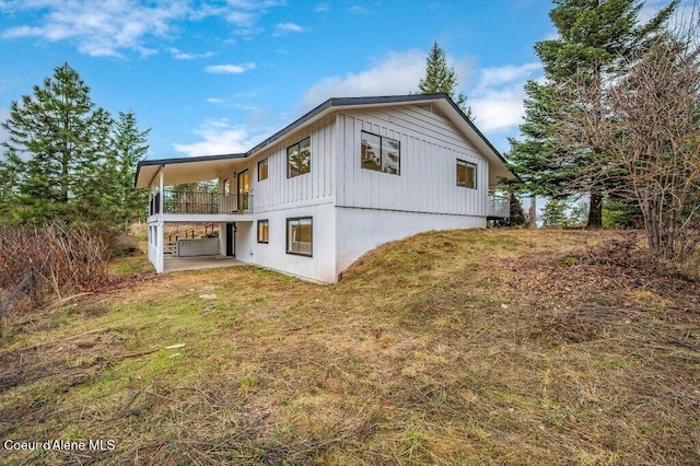 rear view of property featuring board and batten siding, a patio area, a lawn, and a balcony