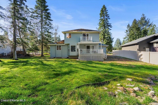 rear view of house featuring a yard, fence, and a balcony