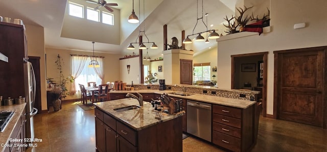 kitchen featuring a sink, ceiling fan, appliances with stainless steel finishes, a towering ceiling, and a center island with sink