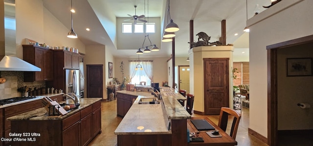 kitchen with ceiling fan, high vaulted ceiling, wall chimney range hood, a sink, and a spacious island