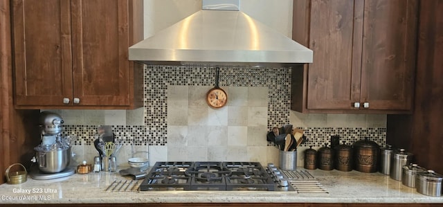 kitchen featuring stainless steel gas cooktop, light stone counters, decorative backsplash, and exhaust hood