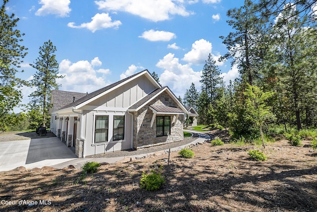 back of house with board and batten siding, driveway, a garage, and stone siding