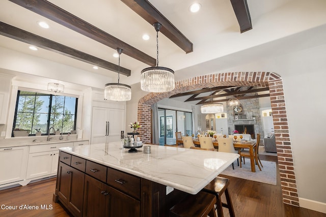 kitchen featuring a sink, beamed ceiling, light stone counters, and dark wood finished floors
